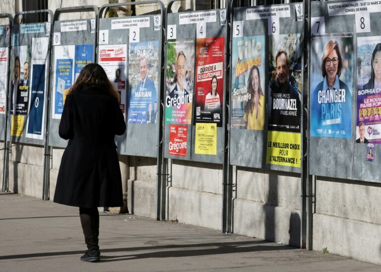 Une femme passe devant un panneau électoral avec les candidats à la mairie de Paris, le 9 mars 2026, à Paris © Ludovic MARIN