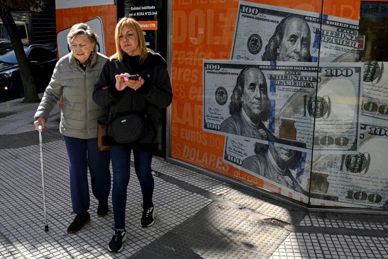 Des femmes passent devant une image de billets de cent dollars, à Buenos Aires le 14 août 2023 © Luis ROBAYO