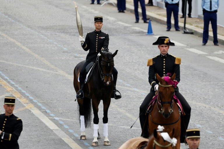 Le cavalier Thibaut Vallette (c), chef des écuyers du Cadre noir de Saumur et médaillé d'or aux JO de Rio en 2016, porte la flamme olympique lors du défilé militaire avenue Foch, le 14 juillet 2024 à Paris © Ludovic MARIN