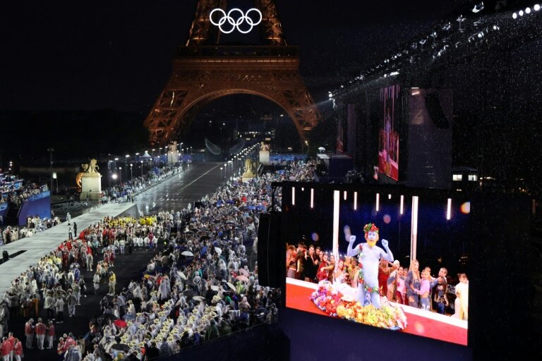 Les délégations arrivent au Trocadéro alors que les spectateurs regardent le chanteur français Philippe Katerine se produire sur un écran géant lors de la cérémonie d'ouverture des JO-2024 à Paris le 26 juillet 2024 © Ludovic MARIN