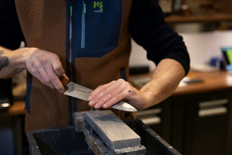 Flavien Walterscheid affûte un couteau sur une pierre japonaise le 25 février 2025 dans son bar à couteaux à Paris © Thomas SAMSON