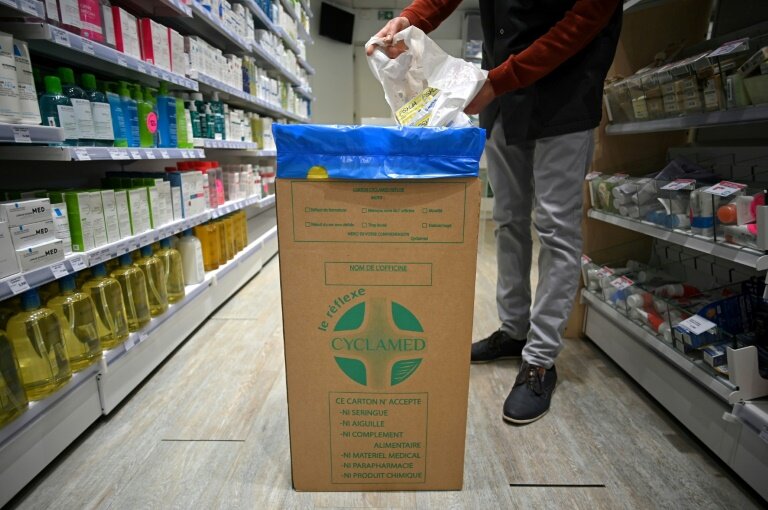 Un homme jette des médicaments non utilisés dans une boîte en carton de l'organisme Cyclamed, chargé de leur collecte, le 23 mars 2023 dans une pharmacie à Colomiers © Valentine CHAPUIS