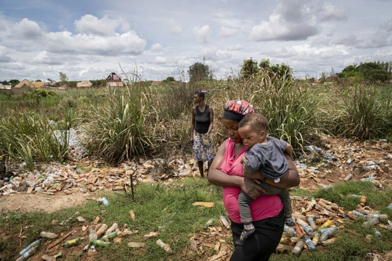 Hélène Mvubu porte sa fille en marchant dans un champ pollué à Lubumbashi en République démocratique du Congo le 24 novembre 2025 © Glody MURHABAZI