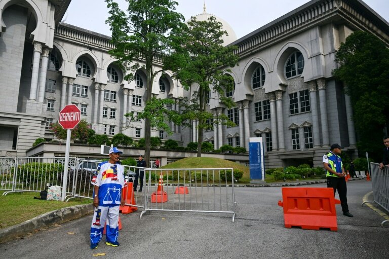 Un partisan de l'ex-Premier ministre malaisien Najib Razak (à gauche), habillé aux couleurs de son parti, se tient devant le palais de justice de Putrajaya, en Malaisie, le 26 décembre 2025 © Mohd RASFAN