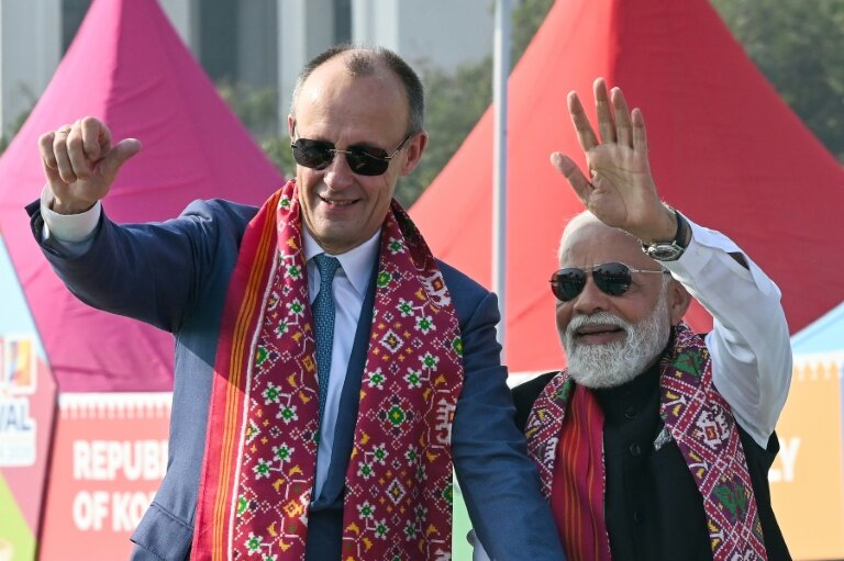 Le Premier ministre indien Narendra Modi (d) et le chancelier allemand Friedrich Merz saluent la foule à leur arrivée au Festival international de cerfs-volants d'Ahmedabad, le 12 janvier 2026 © Shammi MEHRA