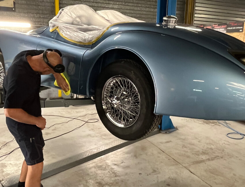 Un compagnon de l’Atelier des Coteaux peaufine les finitions d’un cabriolet de collection sur le pont élévateur, illustrant le souci permanent du détail.