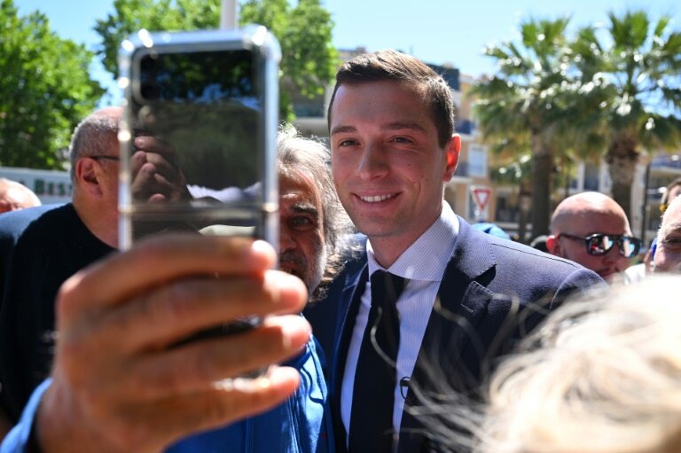 Jordan Bardella, président du RN et tête de liste aux élections européennes, pose pour un selfie avec un partisan lors d'une visite de campagne dans un marché en plein air de la ville de Sainte-Maxime, le 31 mai 2024 © Nicolas TUCAT