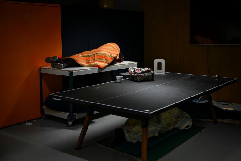 Des personnes dorment sur ou sous des tables à l'intérieur de la Gaîte Lyrique à Paris, le 11 décembre 2024 © Grégoire CAMPIONE