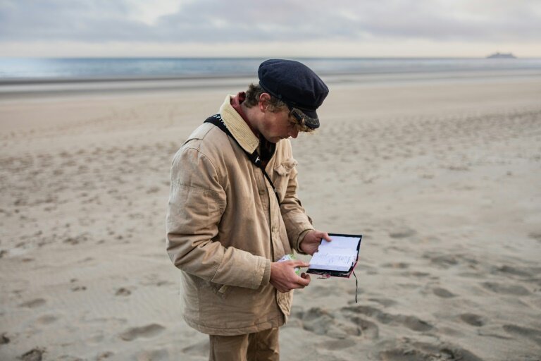 Le "beachcomber" belge Aäron Fabrice de Kisangani regarde un carnet abandonné par des migrants sur la plage de Gravelines, le 26 mars 2025 dans le Nord © Sameer Al-DOUMY