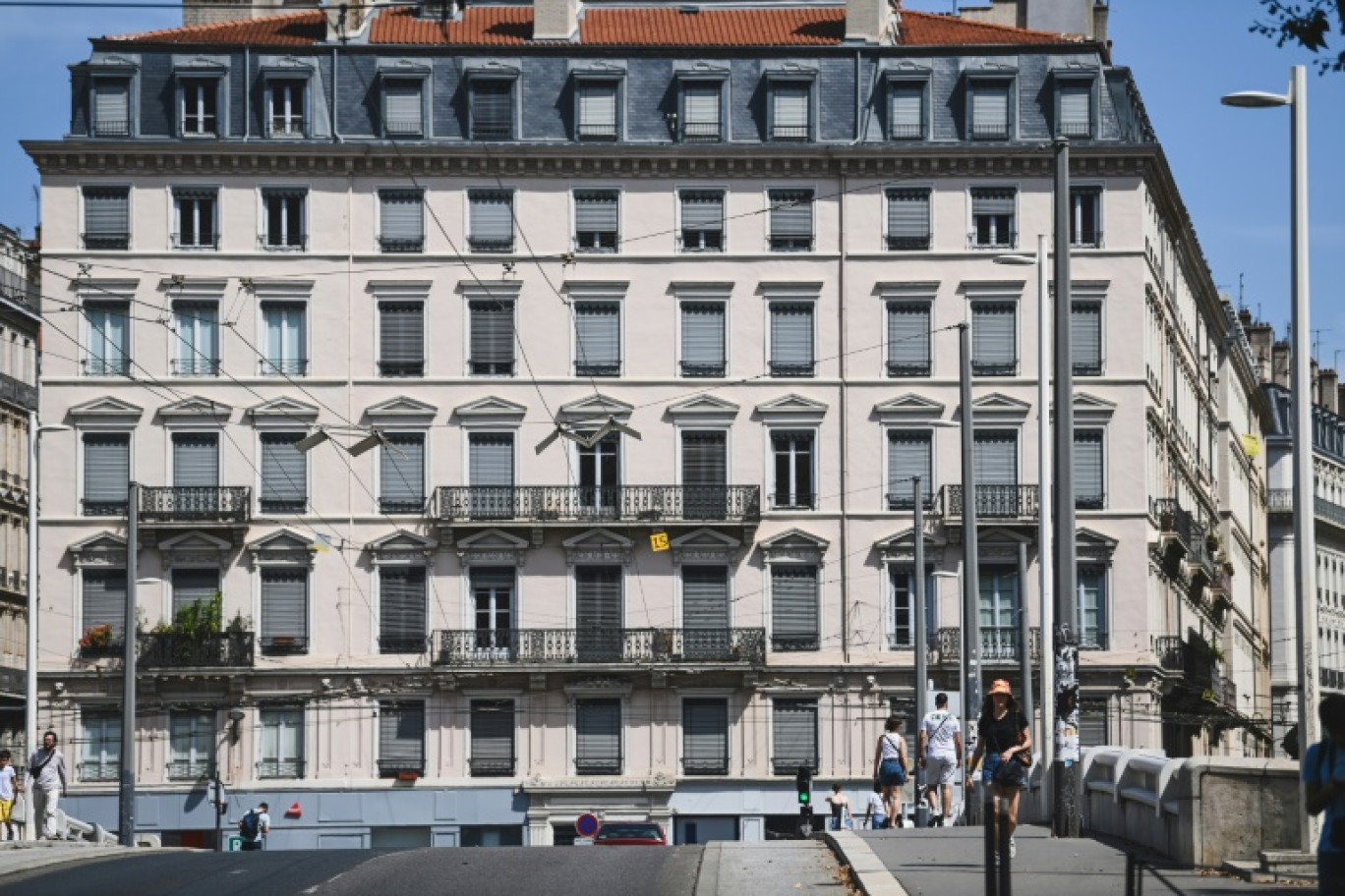 Des piétons passent à proximité d'un immeuble aux volets fermés en raison de la vague de chaleur, le 18 août 2023 à Lyon © OLIVIER CHASSIGNOLE