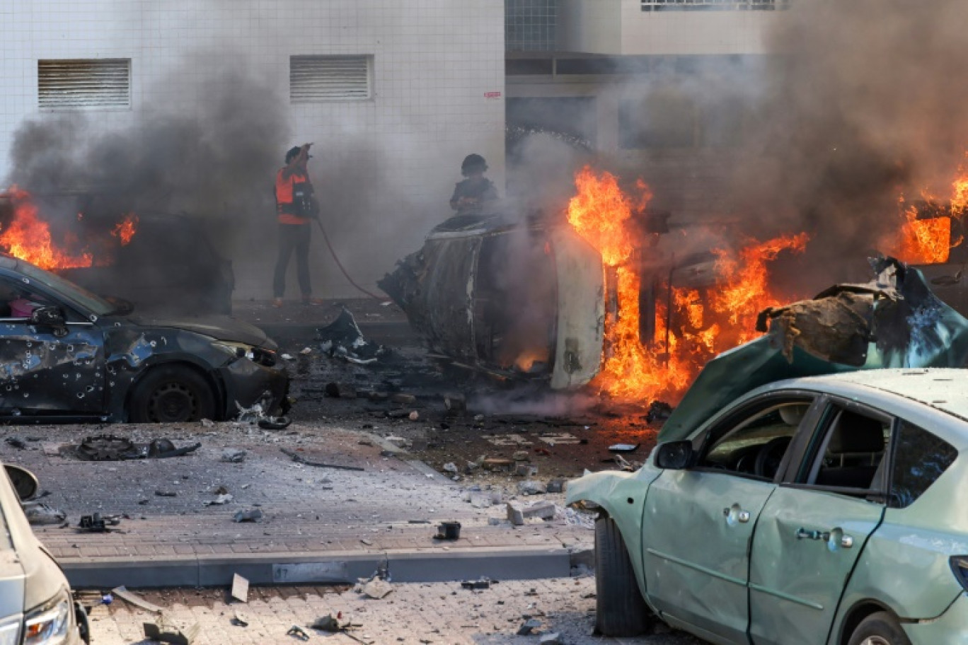 Des habitants tentent d'éteindre des véhicules en flammes au pied d'un immeuble résidentiel à Ashkelon, après des tirs de roquettes depuis la bande de Gaza vers Israël, le 7 octobre 2023 © AHMAD GHARABLI
