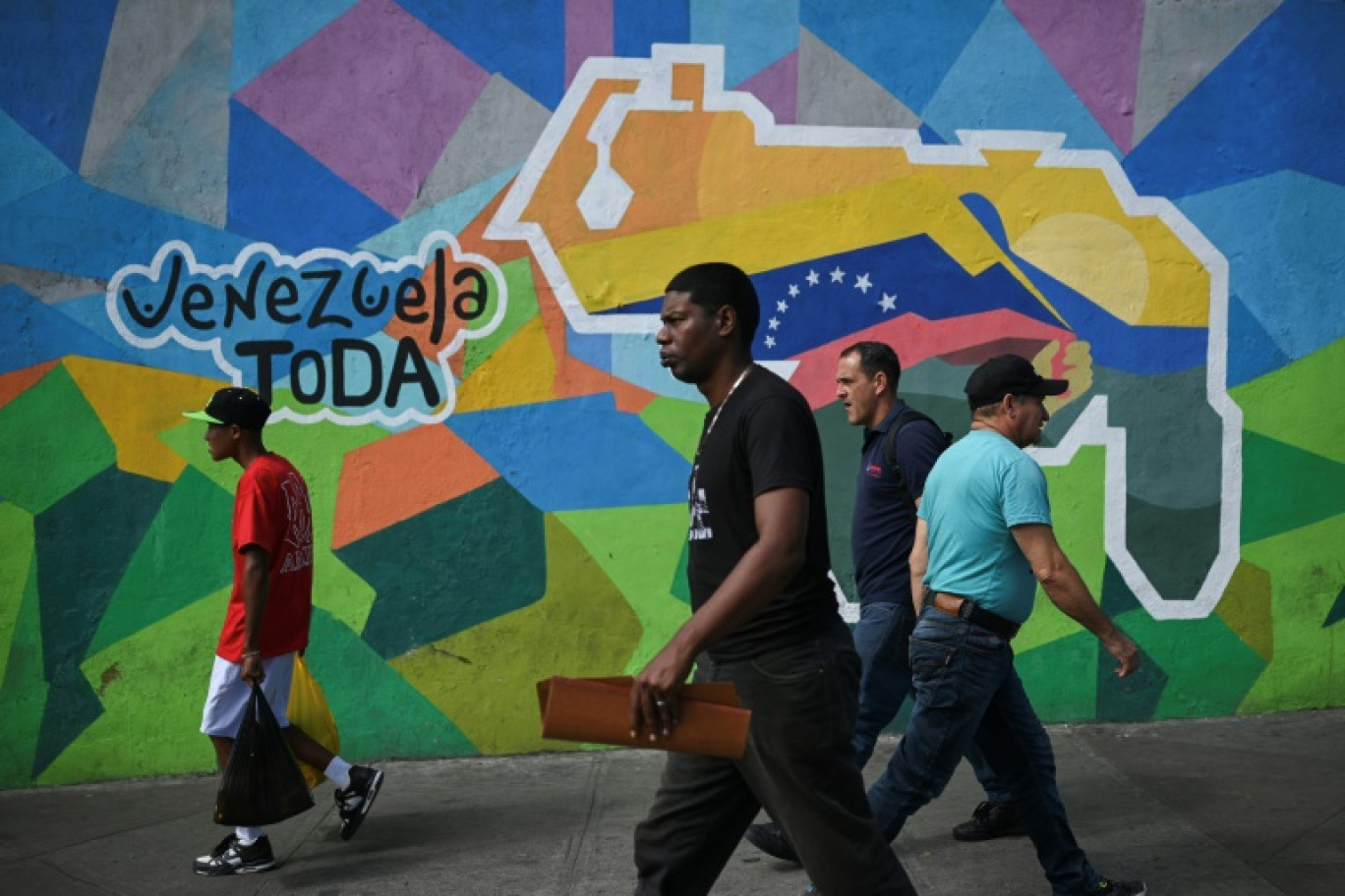 Des personnes passent devant une fresque murale faisant campagne pour un référendum demandant aux Vénézuéliens d'envisager l'annexion de la région de l'Essequibo administrée par le Guyana voisin, à Caracas, le 28 novembre 2023 © Federico PARRA