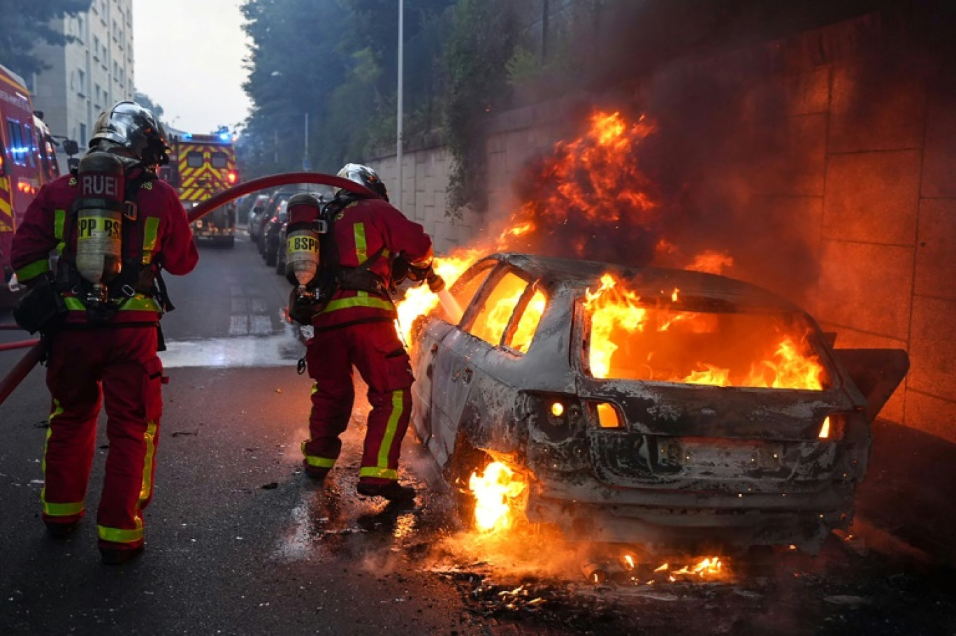Des pompiers tentent d'éteindre une voiture en feu en marge d'une manifestation à Nanterre, théâtre d'incidents en soirée, le 27 juin 2023 © Zakaria ABDELKAFI