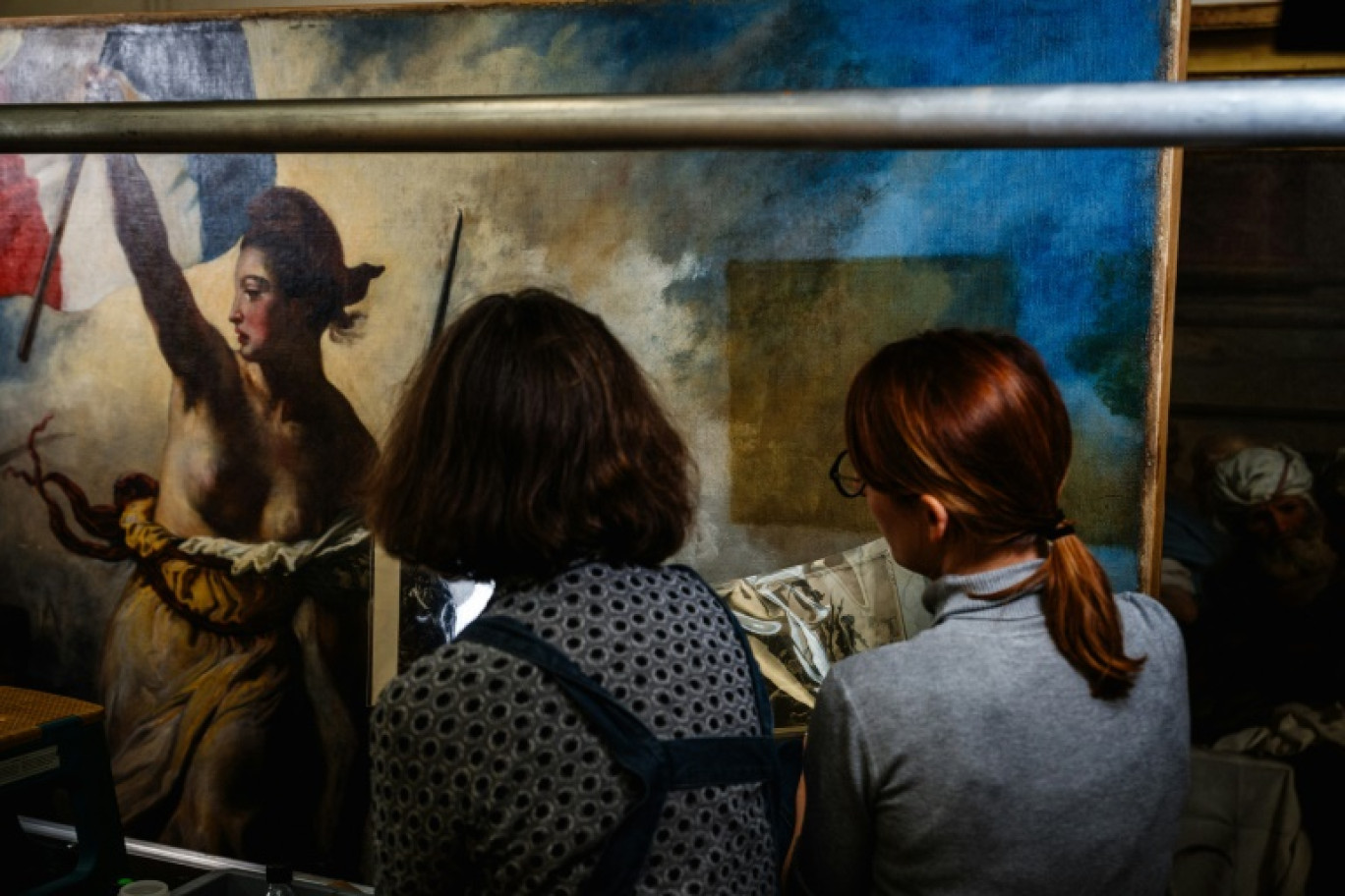 Des restaurateurs travaillent sur le tableau "La liberté guidant le peuple" d'Eugène Delacroix, dans un laboratoire du Musée du Louvre à Paris, le 28 février 2024 © Dimitar DILKOFF