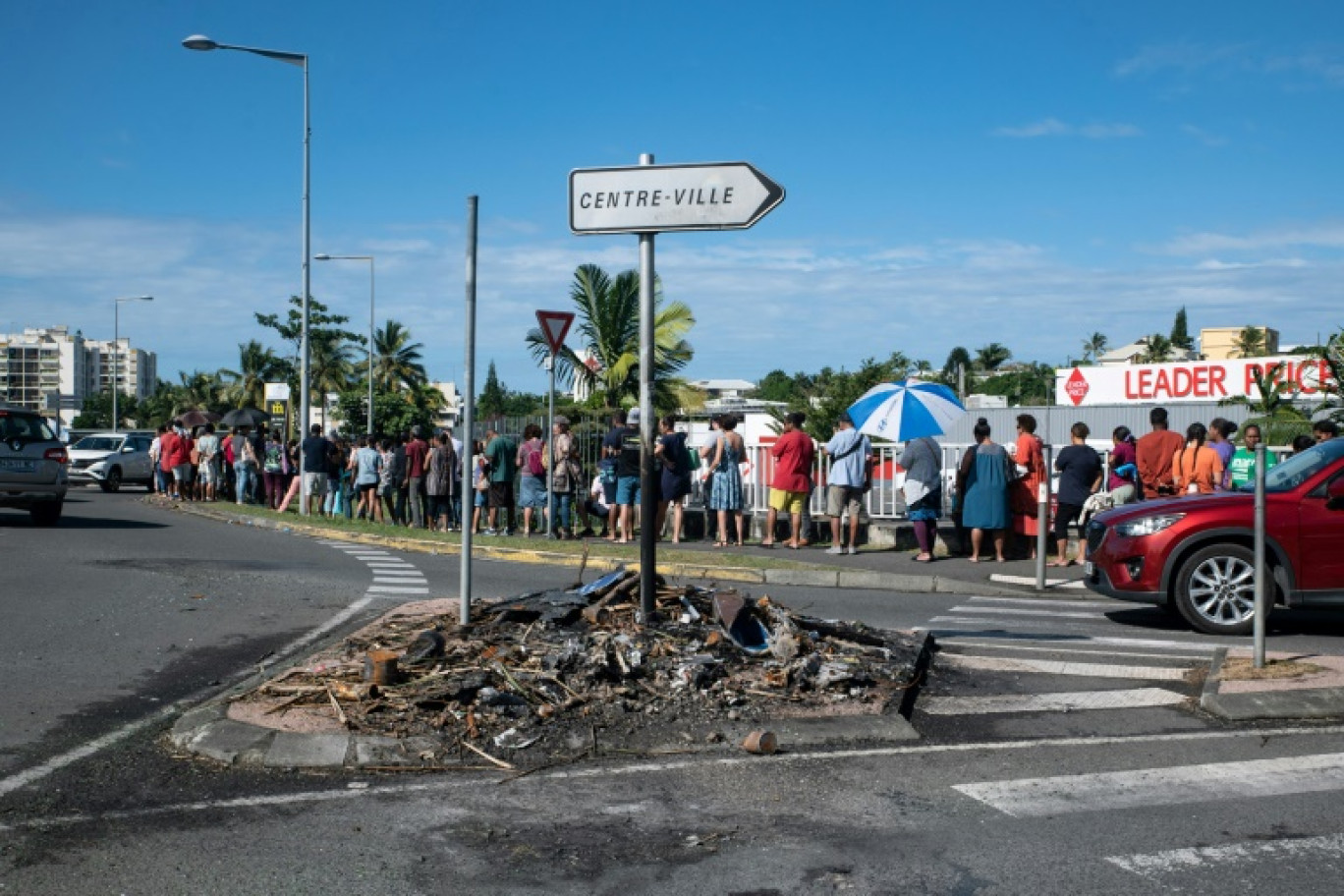 Des habitants font la queue pour acheter des provisions dans un supermarché, à côté des restes incendiés des incidents de la nuit, dans le quartier de Magenta à Nouméa, en Nouvelle Calédonie le 18 mai 2024 © Delphine Mayeur