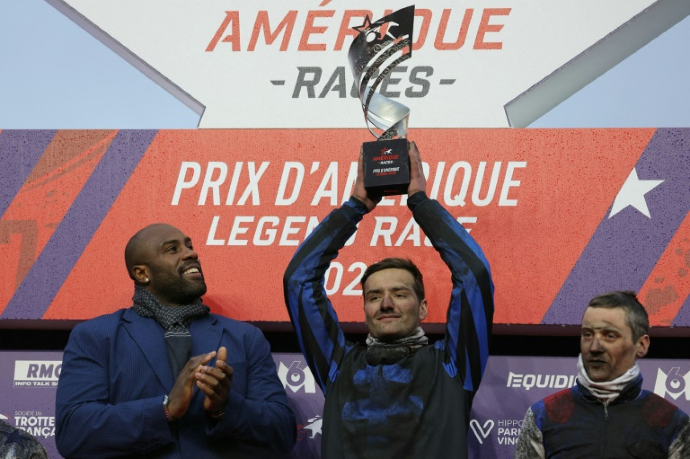 Clément Duvaldestin brandit son trophée aux côtés du judoka Teddy Riner et de Romain Derieux, après avoir remporté le 104e Prix d'Amérique à l'Hippodrome de Vincennes à Paris le 26 janvier 2025 © THOMAS SAMSON