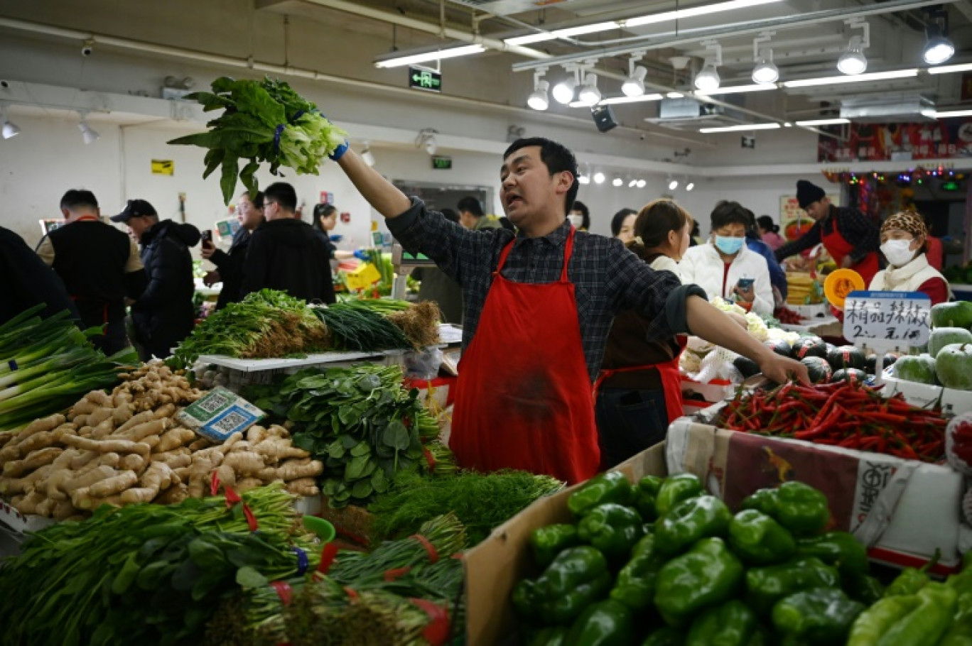 Un vendeur de légumes harangue les clients sur un marché de Pékin, le 9 mars 2025 © GREG BAKER