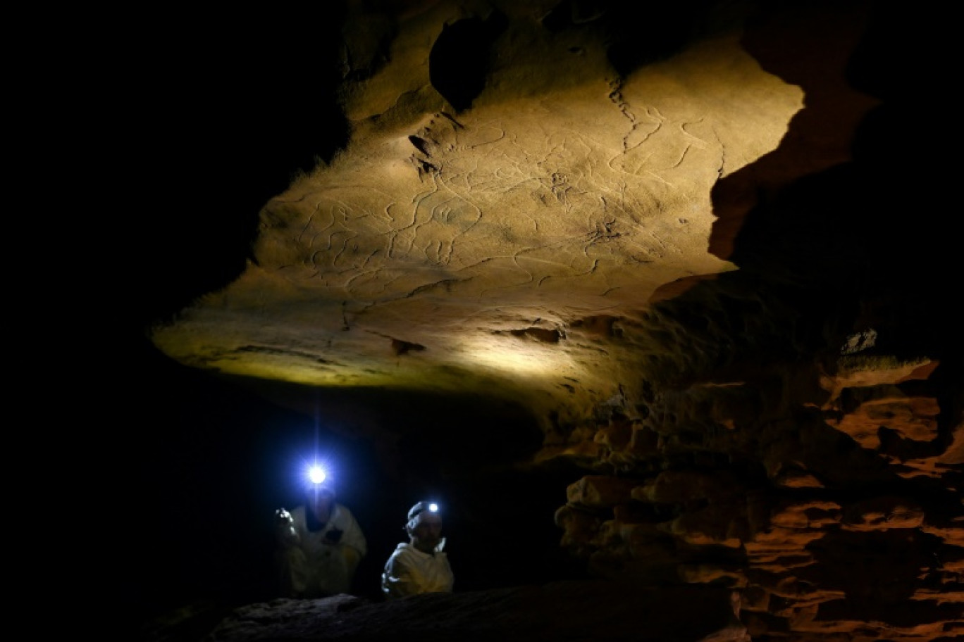 Des scientifiques éclairent avec leurs torches des gravures sur roche datant d'environ 30 000 ans lors d'une visite exclusive accordée par la DRAC de Nouvelle-Aquitaine, à l'intérieur de la grotte de Cussac, le 20 février 2025 au Buisson-de-Cadouin, en Dordogne © Christophe ARCHAMBAULT