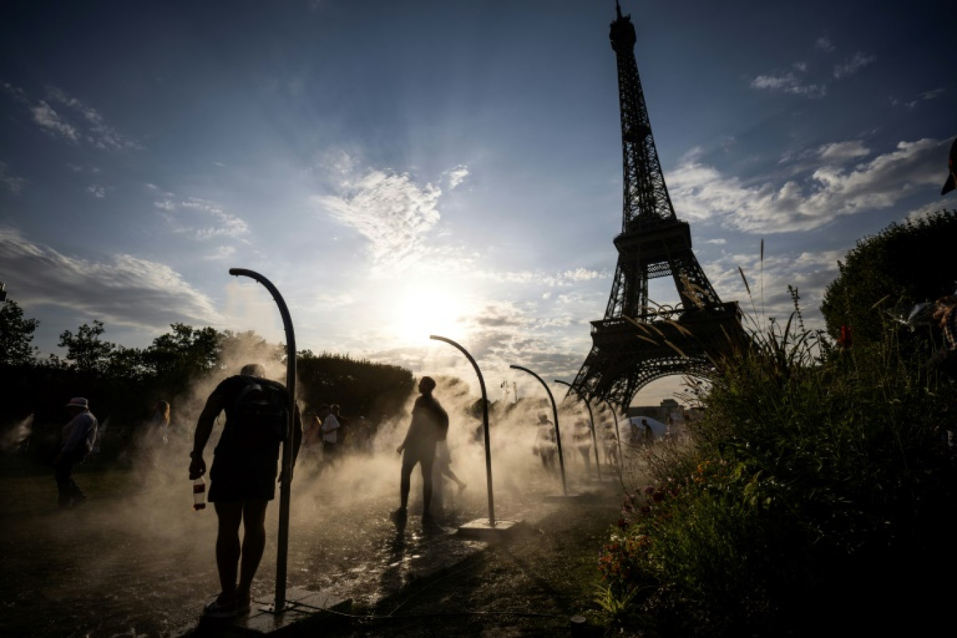 Des passants se rafraîchissent avec des brumisateurs d'eau à côté de la Tour Eiffel à Paris, le 29 juillet 2024 © Luis TATO