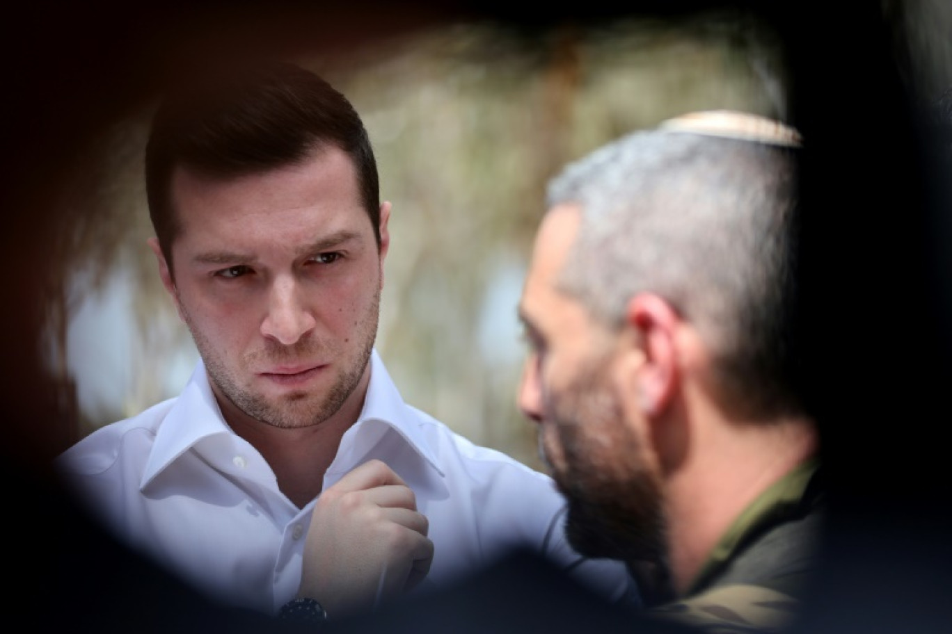 Le président du Rassemblement national (RN), Jordan Bardella (g), écoute l'officier israélien Ethan Dana lors d'une visite au mémorial des victimes et des otages des attaques du 7 octobre 2023, près du kibboutz Re'im dans le sud d'Israël, le 26 mars 2025 © Jack GUEZ