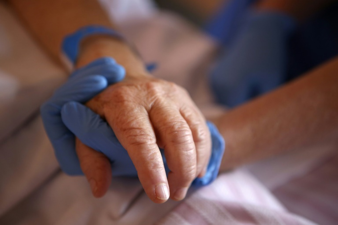 Un personnel soignant tient la main d'un patient en soins palliatifs, à l'hôpital Eugénie d'Ajaccio, le 23 avril 2020 © Pascal POCHARD-CASABIANCA
