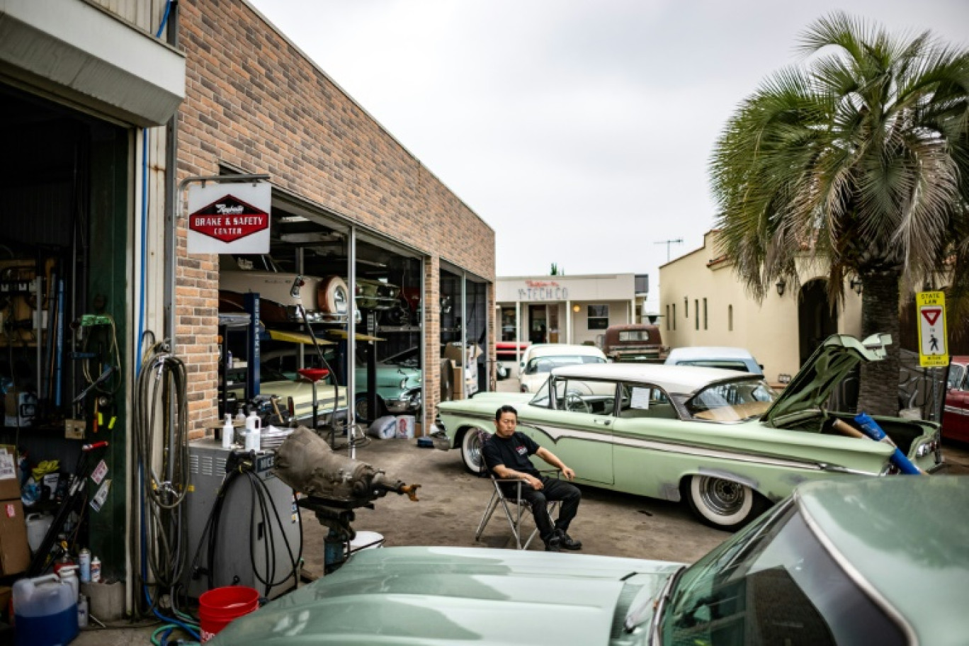 Des voitures importées des Etats-Unis vendue dans le garage de Yosuke Fukuda (c), assis devant son établissement, le 25 avril 2025 à Fukaya, dans la préfecture de Saitama, au Japon © Philip FONG