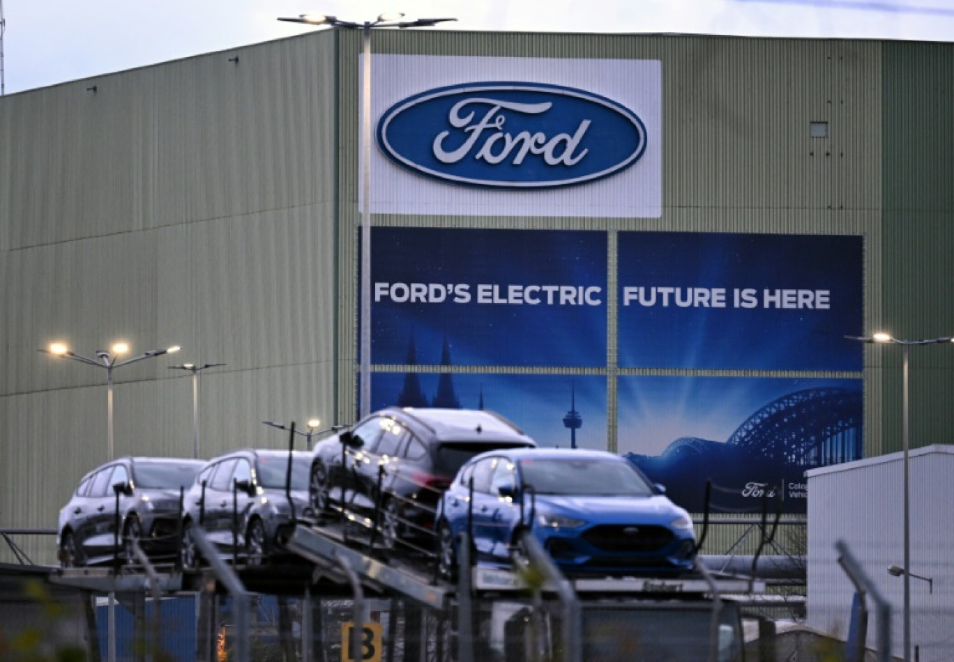 Des voitures du constructeur automobile américain Ford sont alignées sur un camion transporteur devant le logo de l'entreprise à l'usine Ford de Cologne, dans l'ouest de l'Allemagne, le 25 novembre 2024 © Ina FASSBENDER