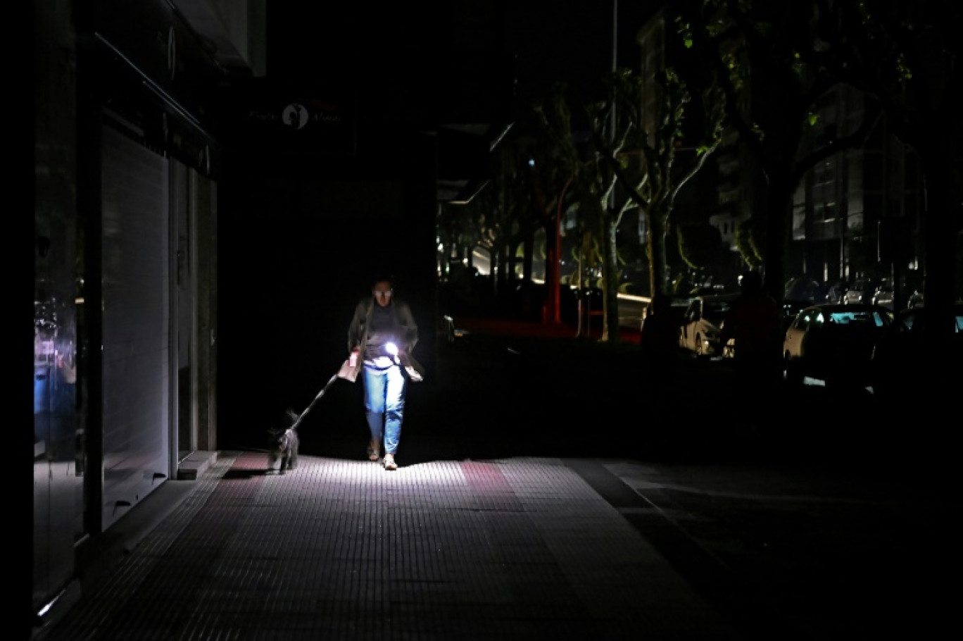 Un passante promène son chien en s'éclairant avec son téléphone, le 28 avril 2025 à Vigo, dans le nord-ouest de l'Espagne, pendant une panne d'électricité géante © MIGUEL RIOPA