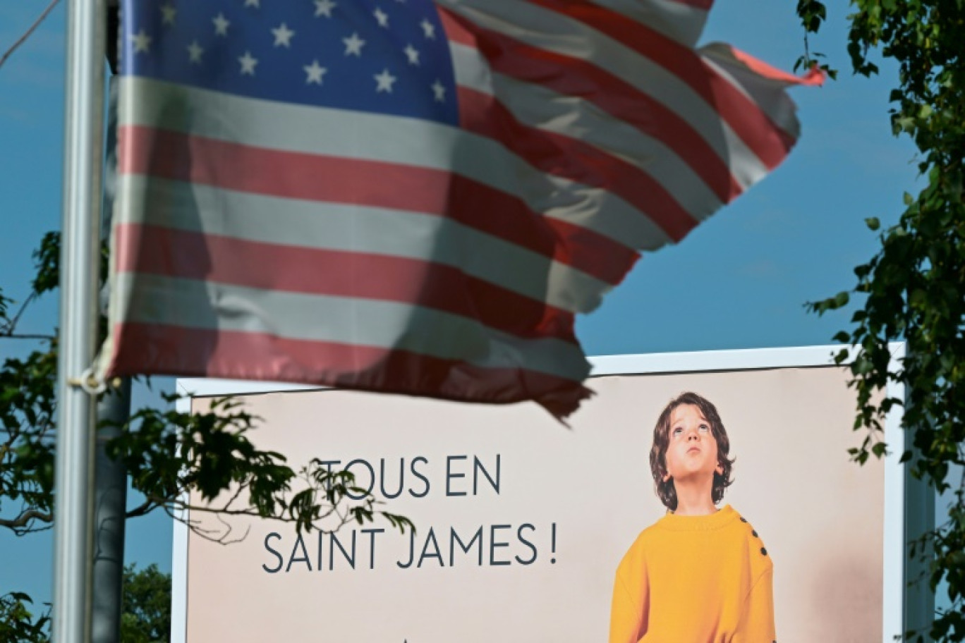 Une affiche publicitaire derrière un drapeau américain à côté de l'usine Saint-James, dans la Manche, le 22 mai 2025 © Damien MEYER