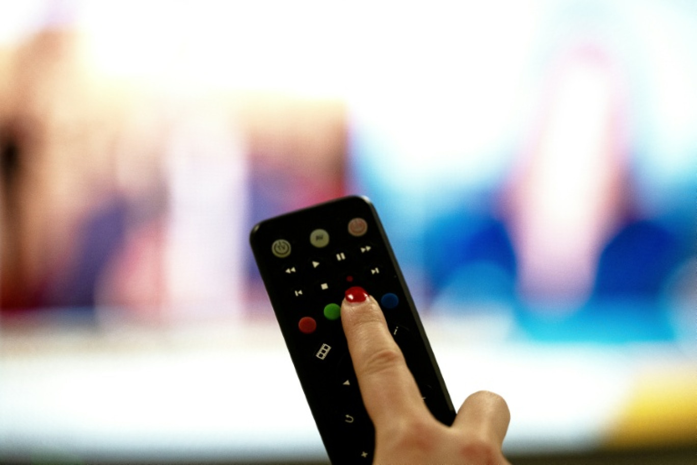 Une personne tient une télécommande pointée vers un écran de télévision, à Paris le 15 janvier 2025 © Anna KURTH