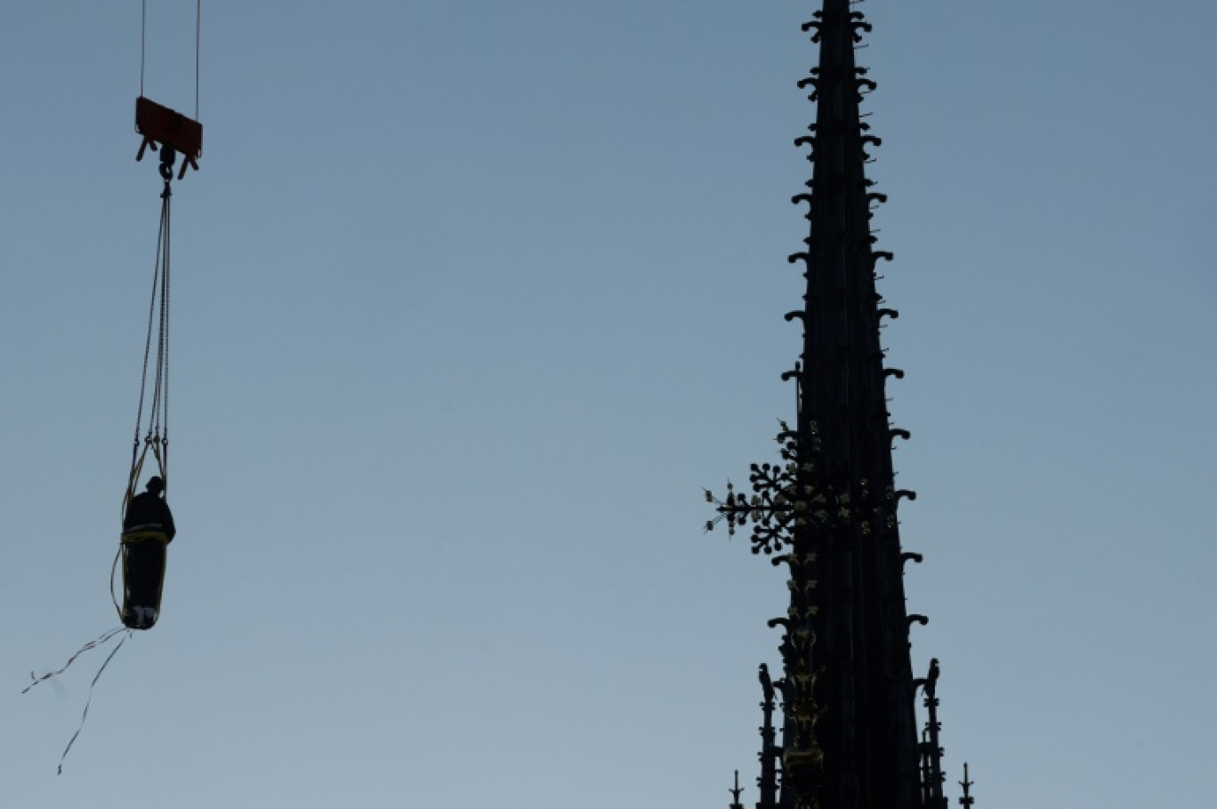 Une grue soulève l'une des 16 statues géantes d'apôtres pour la replacer sur sa base au pied de la flèche de la cathédrale Notre-Dame de Paris, le 23 juin 2025 © GEOFFROY VAN DER HASSELT