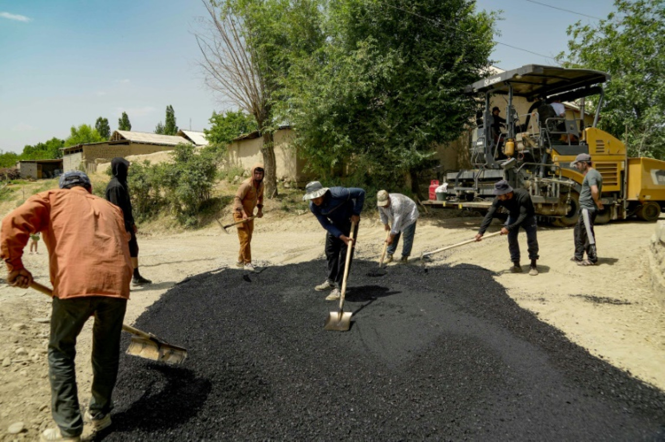 Des ouvriers asphaltent une route dans le village de Mehrobod, un projet de développement financé par des migrants tadjiks à l'étranger, le 25 mai 2025 au Tadjikistan © STRINGER