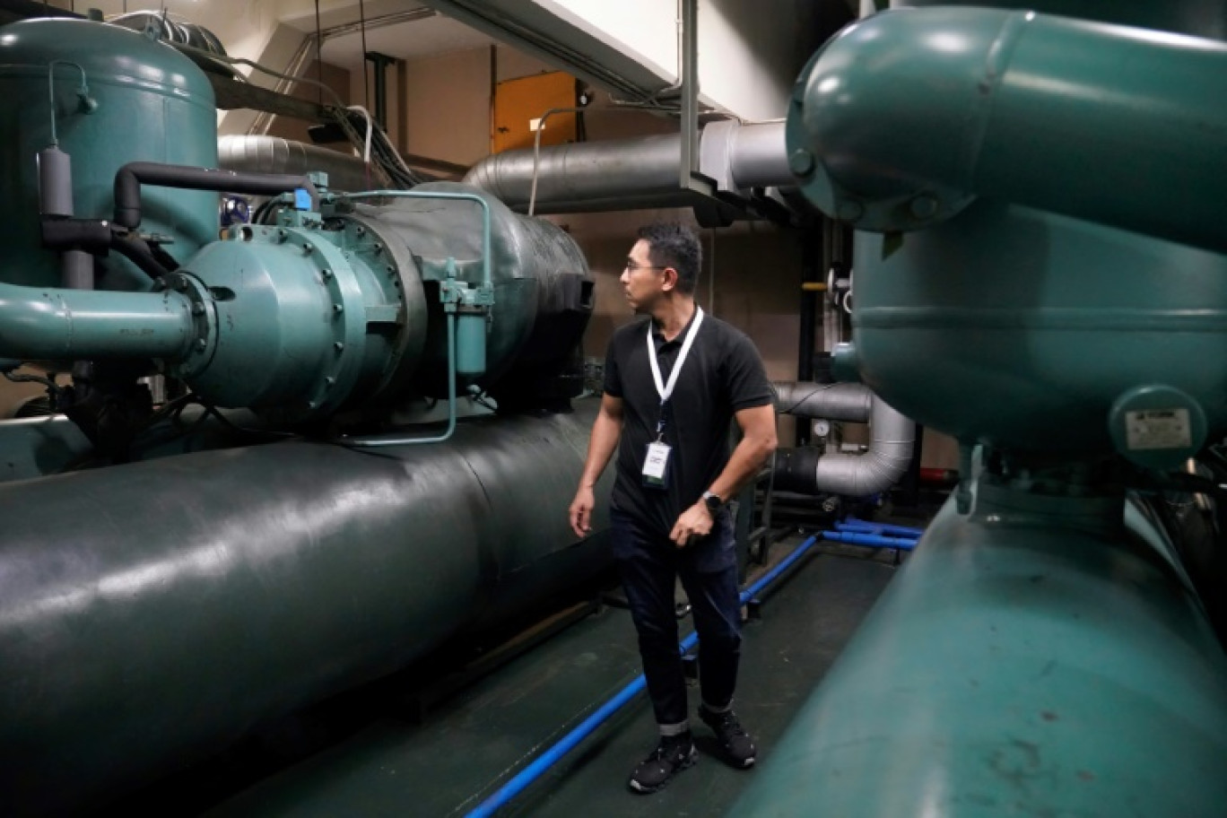 Un technicien de la société Recoolit travaille à capturer les gaz de refroidissemen d'une grande unité de climatisation au sous-sol d'un complexe d'habitation à Jakarta, le 10 juin 2025 en Indonésie © Jack Moore