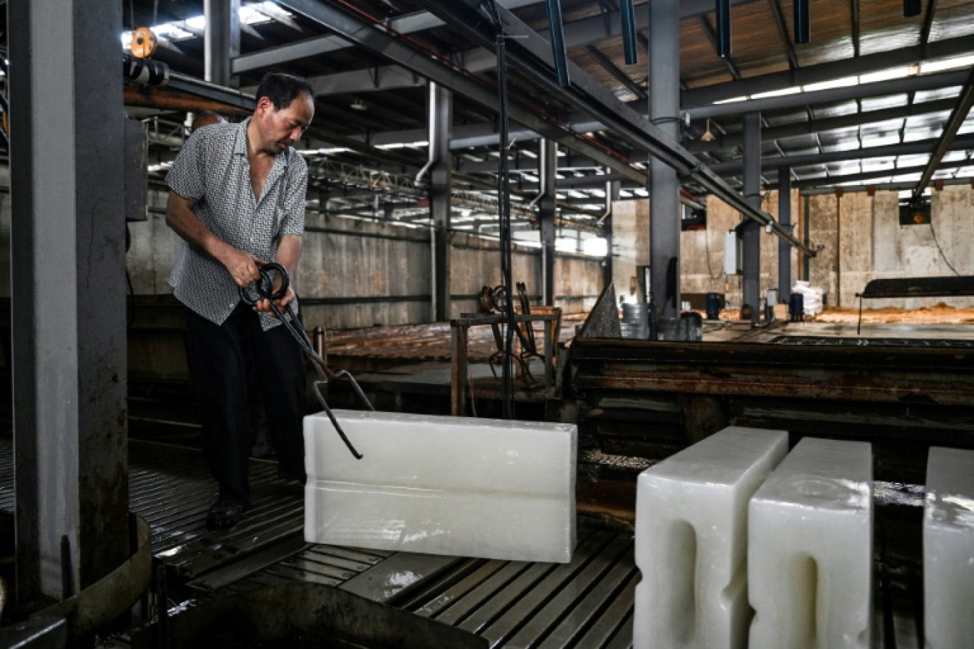 Un ouvrier transporte des blocs de glace vers un camion réfrigéré à l'usine de production de glace Feichao à Hangzhou, dans la province orientale du Zhejiang, le 9 juillet 2025 en Chine © Hector RETAMAL