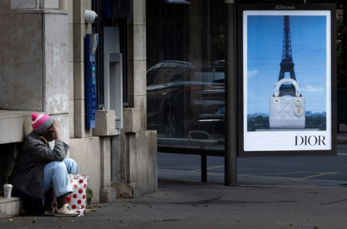 Une personne sans abri à Paris, devant une publicité pour une marque de luxe, le 8 juillet 2025 © JOEL SAGET