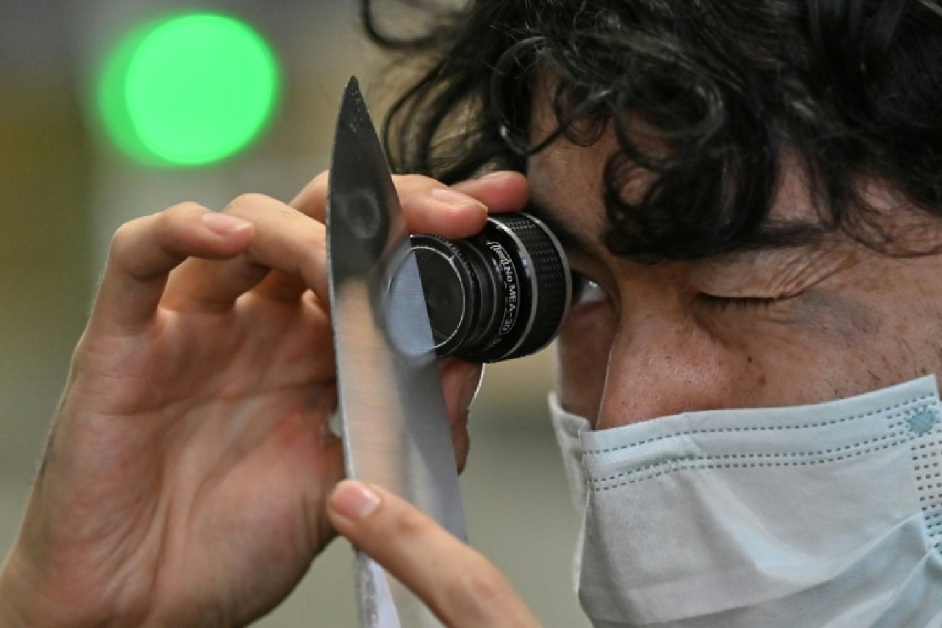 Un employé du fabricant japonais de couteaux Sumikama inspecte une lame à l'aide d'une loupe dans son usine de Seki, au Japon, le 22 juillet 2025 © Richard A. Brooks
