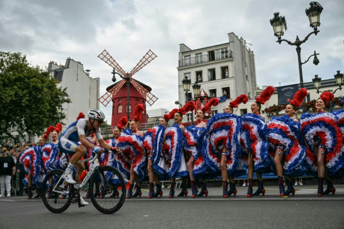 Le cycliste rançais Valentin Madouas passe devant les danseuses du Moulin-Rouge lors des Jeux olympiques de Paris, le 3 août 2024 à Paris © Mauro PIMENTEL