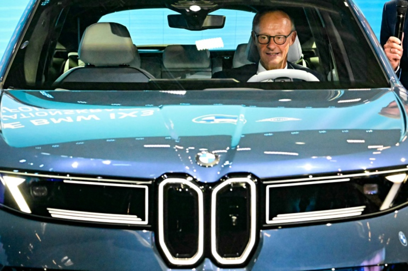 Le chancelier allemand Friedrich Merz assis dans une BMW IX3 sur le stand du constructeur automobile lors de l'ouverture du Salon international de l'automobile IAA, le 9 septembre 2025 à Munich, dans le sud de l'Allemagne © Tobias SCHWARZ