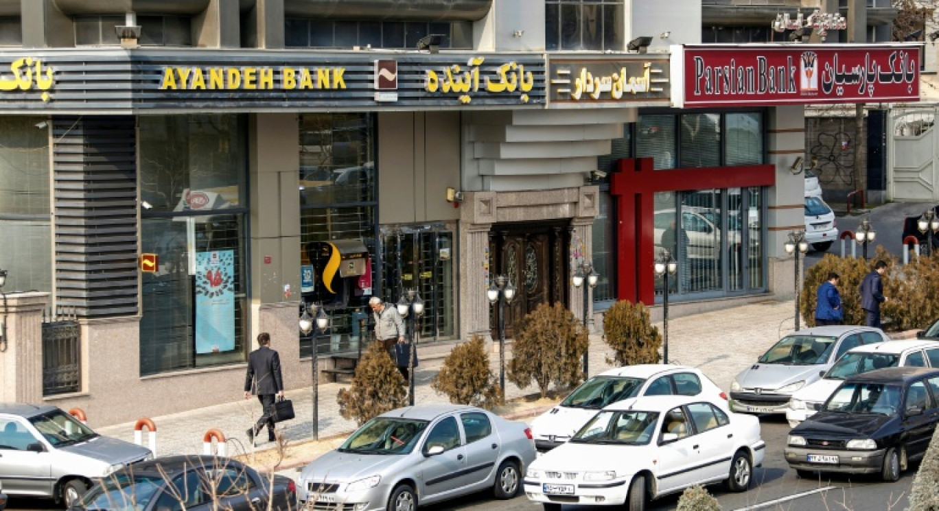 Des Iraniens passent devant une succursale de la banque Ayandeh (G) dans la capitale Téhéran, le 14 janvier 2017 © ATTA KENARE