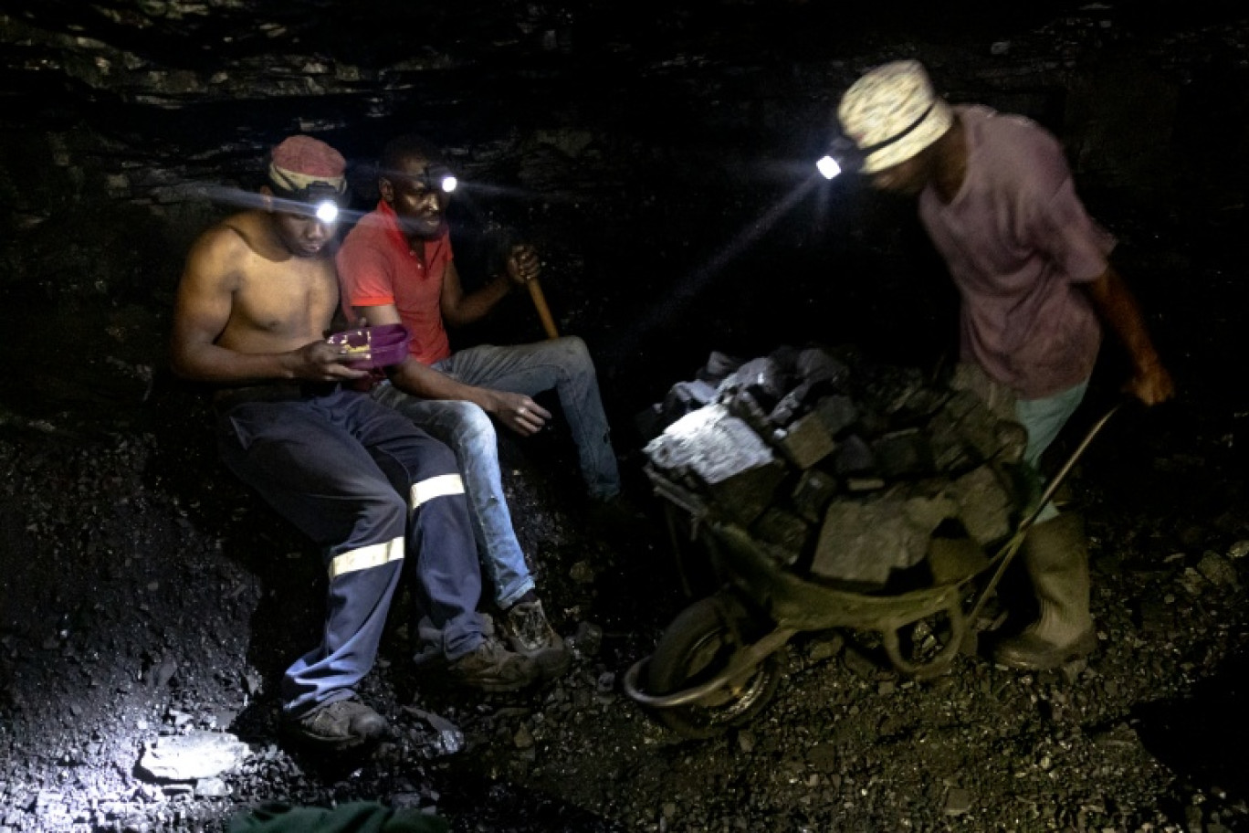 Des mineurs illégaux font une pause tandis qu'un autre pousse une brouette remplie de charbon dans la mine de Golfview à Ermelo le 25 septembre 2025, en Afrique du Sud © EMMANUEL CROSET