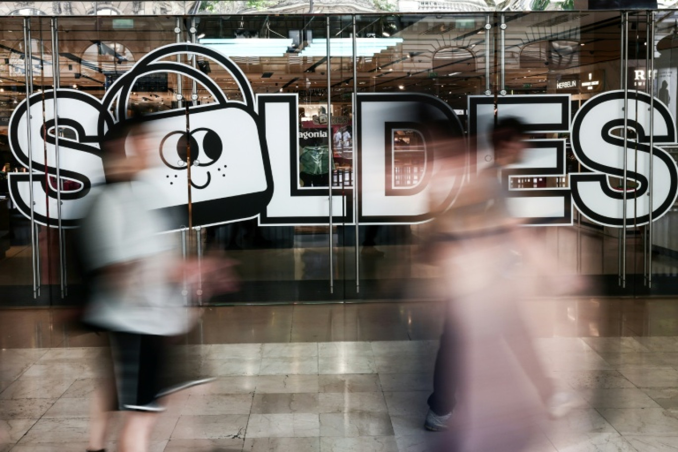 Des passants marchent à proximité de l'entrée d'un centre commercial annonçant les soldes, le 25 juin 2025 à Paris © Thibaud MORITZ