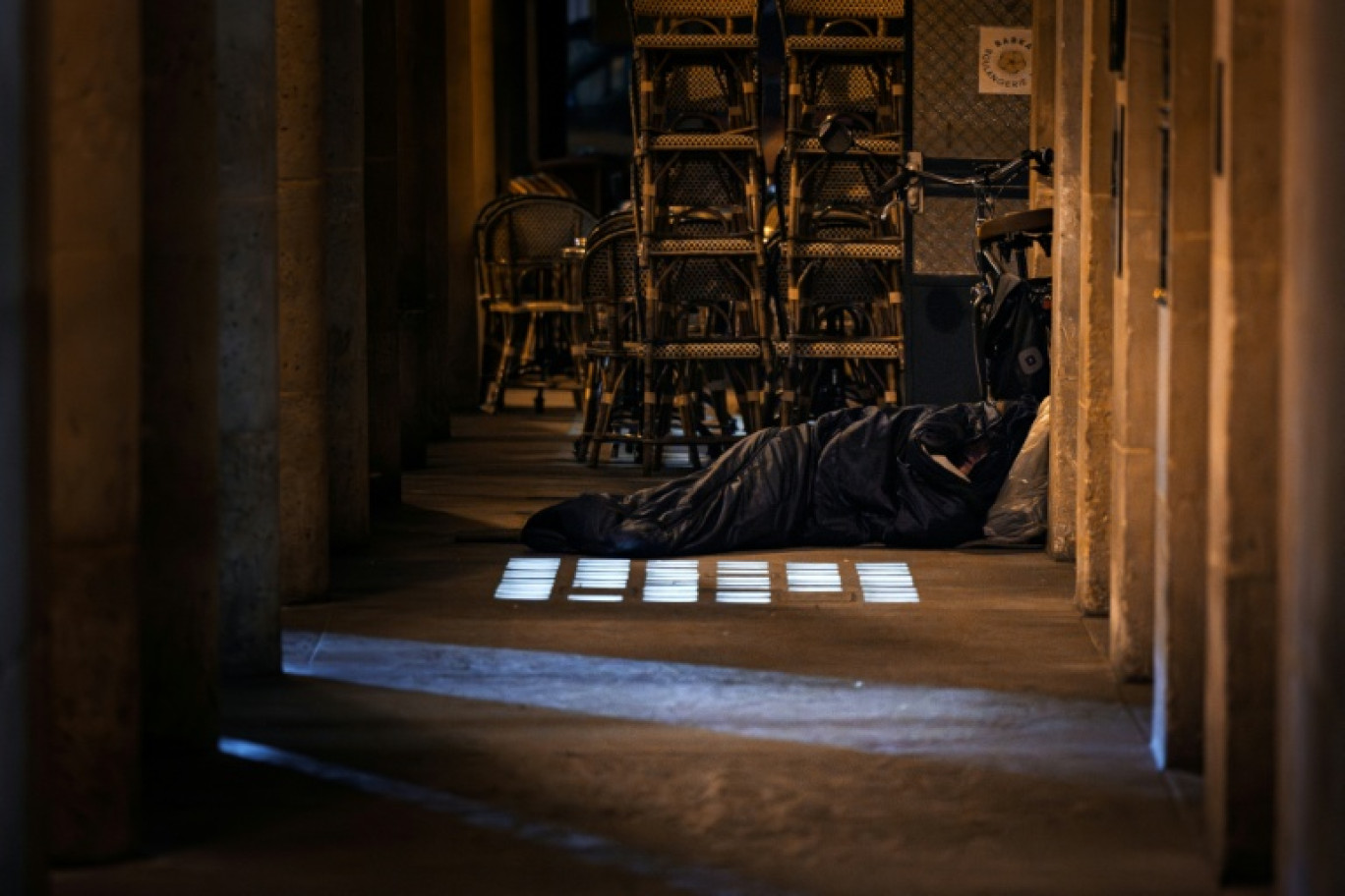 Un sans-abri dort dans un sac de couchage à côté de la terrasse d'un café à Paris, le 15 octobre 2025 © JOEL SAGET