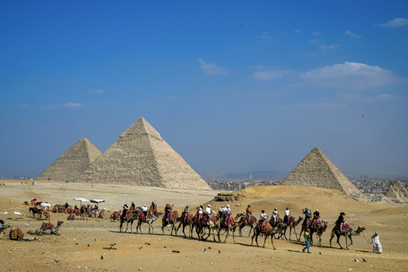 Des touristes à dos de chameau visitent la nécropole des pyramides de Gizeh, le 7 novembre 2025 en Egypte © Khaled DESOUKI